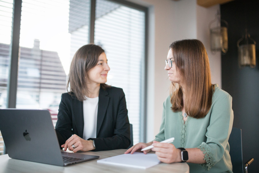 Zwei Frauen im Büro vor einem Laptop lächeln sich an